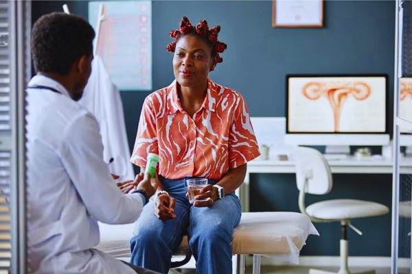 Smiling Black woman in a medical consultation with her doctor, discussing treatment options and medication for managing Premature Ovarian Failure (POF)