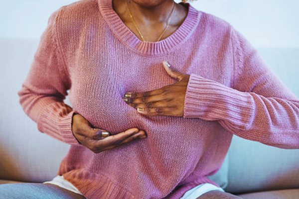 Young African woman experiencing ovulation breast pain, gently touching her chest with a concerned expression during her menstrual cycle